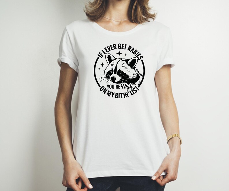 May include: White t-shirt with a black graphic of a raccoon inside a circle, with the text "If I ever get rabies you're high on my bitin' list". The raccoon has a detailed face.