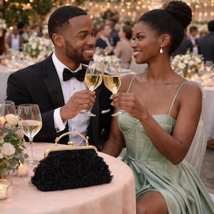 May include: A black evening bag with a gold handle and a rose design sits on a table. A couple is toasting with champagne glasses. The woman wears a sage green dress, and the man wears a black tuxedo with a bow tie. The scene is set at an outdoor event.