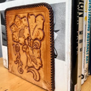 May include: A brown leather bookend with a floral design. The bookend is holding up a stack of books with titles like "Atlas of the Universe", "Stamping and Understanding Abstract Art", and "Modern Paper".
