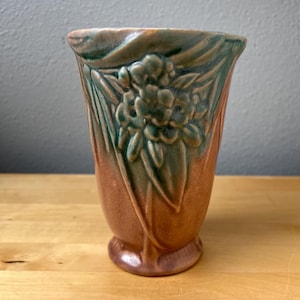 May include: A vintage ceramic vase with a floral design. The vase features a two-tone color scheme, with a brown base and green accents. The embossed floral pattern adds a touch of elegance to this decorative piece.