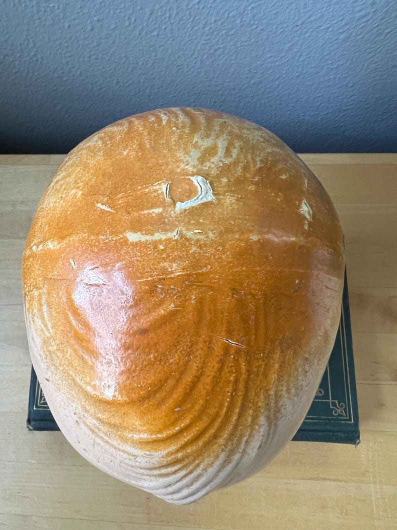 May include: A large, rounded ceramic vessel with a warm, earthy color palette. The exterior features a blend of light tan and rich brown tones, with a glossy finish. The surface has a textured, organic appearance, suggesting a handmade quality. The vessel is likely a decorative piece.