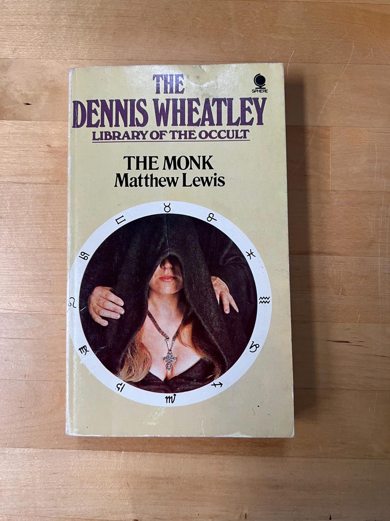 May include: A vintage paperback book titled "The Monk" by Matthew Lewis, part of "The Dennis Wheatley Library of the Occult." The cover features a woman in a dark cloak within a circular design with astrological symbols. The book has a cream-colored background.