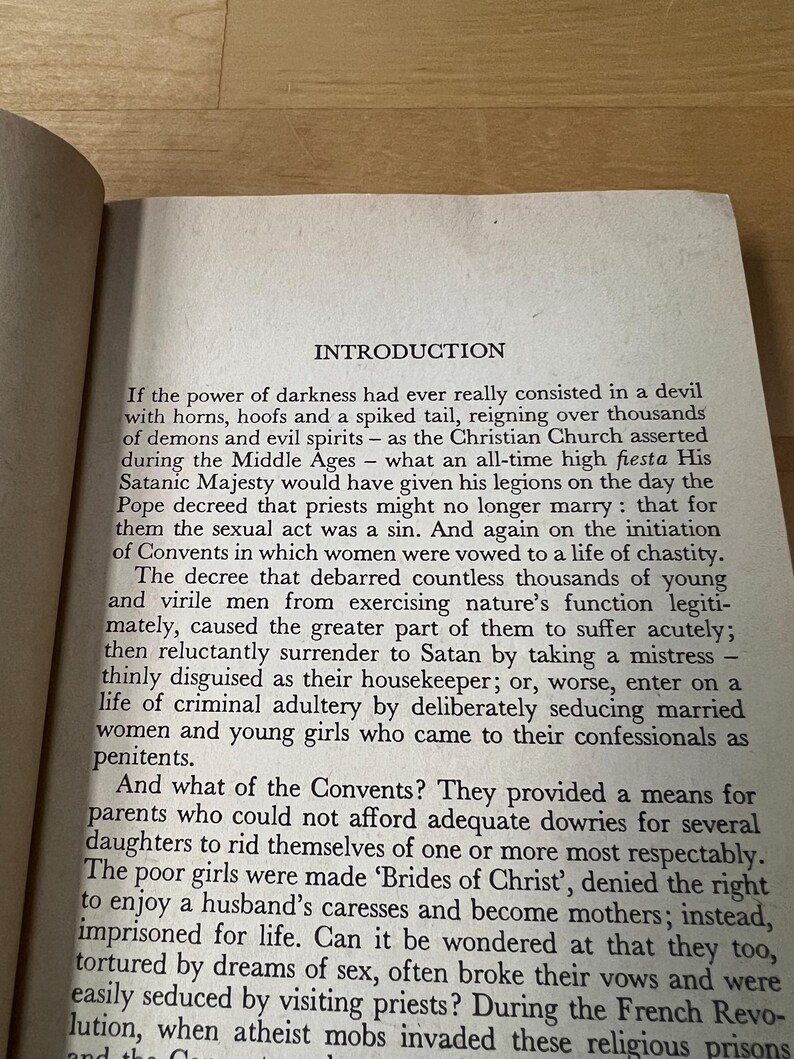 May include: Open book page with text titled "INTRODUCTION". The text is in black font on aged, off-white paper. The page is slightly angled, showing the top and side edges. The text discusses historical views on demons, the church, and convents.