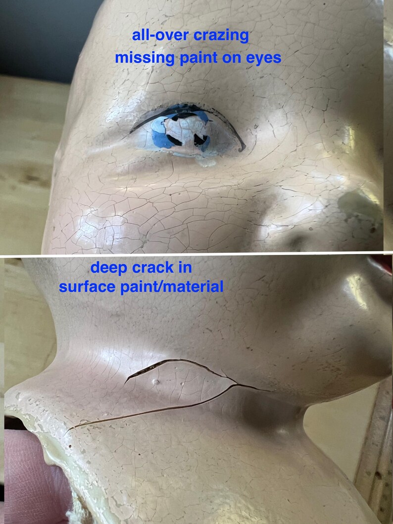 May include: Close-up of a vintage doll's head with visible signs of age. The porcelain surface shows all-over crazing and a deep crack. The doll's eye has missing paint. The text on the image reads: "all-over crazing missing paint on eyes" and "deep crack in surface paint/material".