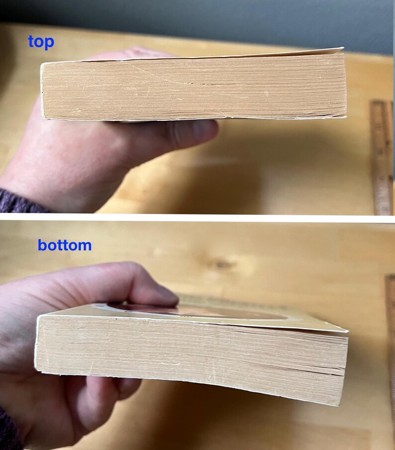 May include: A used book with a tan cover and aged pages. The top and bottom edges of the book are visible, showing the thickness of the pages. The book is held in a person's hand.