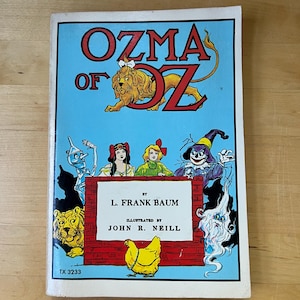 May include: A vintage copy of "Ozma of Oz" by L. Frank Baum, illustrated by John R. Neill. The book cover features a blue background with the title in red and yellow, and illustrations of characters from the story.