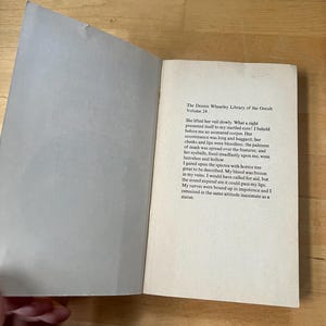 May include: An open book with text from "The Dennis Wheatley Library of the Occult, Volume 24". The pages are off-white with black text. The book is open on a wooden surface.