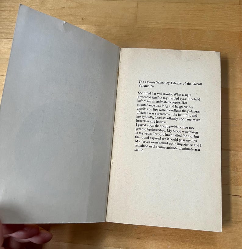 May include: An open book with text from "The Dennis Wheatley Library of the Occult, Volume 24". The pages are off-white with black text. The book is open on a wooden surface.