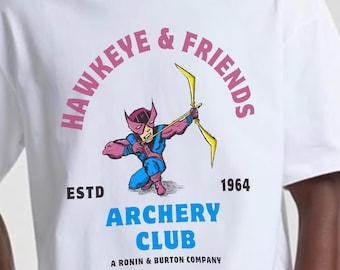 May include: White t-shirt featuring a cartoon illustration of a superhero aiming a bow and arrow. The shirt has the text "HAWKEYE & FRIENDS ARCHERY CLUB" in pink and blue, with "ESTD 1964" below the graphic.