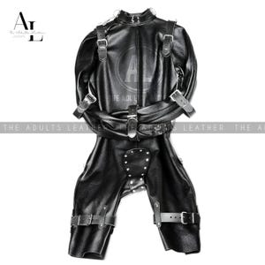 May include: Black leather full body suit with multiple straps and buckles. The suit has a high collar and is designed with a series of straps across the chest and waist. The legs are separate and also have straps. The text "THE ADULTS LEATHER" is visible.