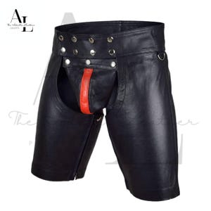 May include: Black leather shorts with a distinctive design. The shorts feature a red accent and silver-tone hardware. The garment has a unique cut with a zipper closure on the side. The shorts are designed for a specific aesthetic.