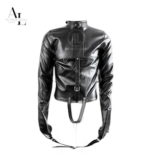 Puede incluir: Chaqueta de cuero negro con mangas largas y cuello alto. La chaqueta tiene cierre de hebilla y correas. Las mangas se extienden hacia abajo con correas que se conectan en las muñecas. El logotipo de The Adults Leather es visible.