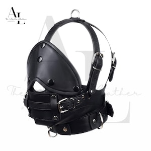 以下が含まれることがあります： 黒い革製のフェイスマスク。パッド入りのアイカバーと口の開口部があります。マスクには、金属製のバックルとDリングが付いた調節可能なストラップが付いています。上部には金属リングがあります。「The Adulte Leather」の文字が左上にあります。