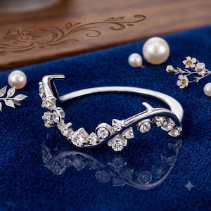 May include: A silver-toned ring featuring a curved, branch-like band adorned with multiple small, round, clear faceted stones. The design mimics a delicate twig, with the stones set along the upper edge of the band in a scattered, organic arrangement.
