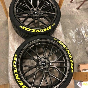 Puede incluir: Dos llantas de aleaci&oacute;n negras con neum&aacute;ticos. Los neum&aacute;ticos tienen la palabra "DUNLOP" en letras amarillas. Las llantas tienen un dise&ntilde;o de radios m&uacute;ltiples y un acabado gris oscuro. Las ruedas est&aacute;n sobre una superficie.