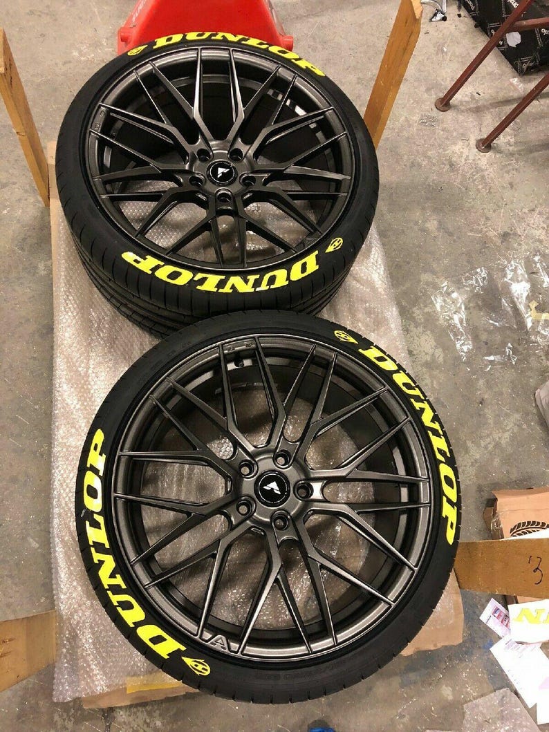 Puede incluir: Dos llantas de aleaci&oacute;n negras con neum&aacute;ticos. Los neum&aacute;ticos tienen la palabra "DUNLOP" en letras amarillas. Las llantas tienen un dise&ntilde;o de radios m&uacute;ltiples y un acabado gris oscuro. Las ruedas est&aacute;n sobre una superficie.