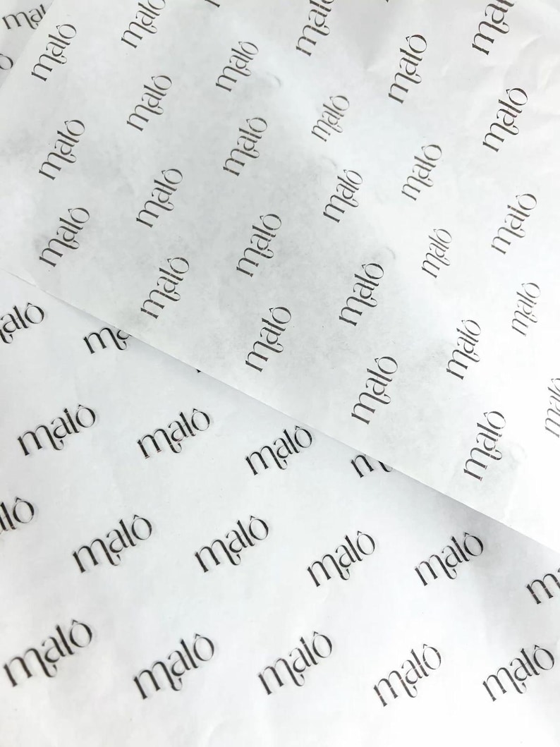 May include: A sheet of thin, semi-translucent white tissue paper featuring a repeating pattern of the word malo printed in a black serif font. The paper is layered, showing multiple sections of the branded material with a soft, creased texture.