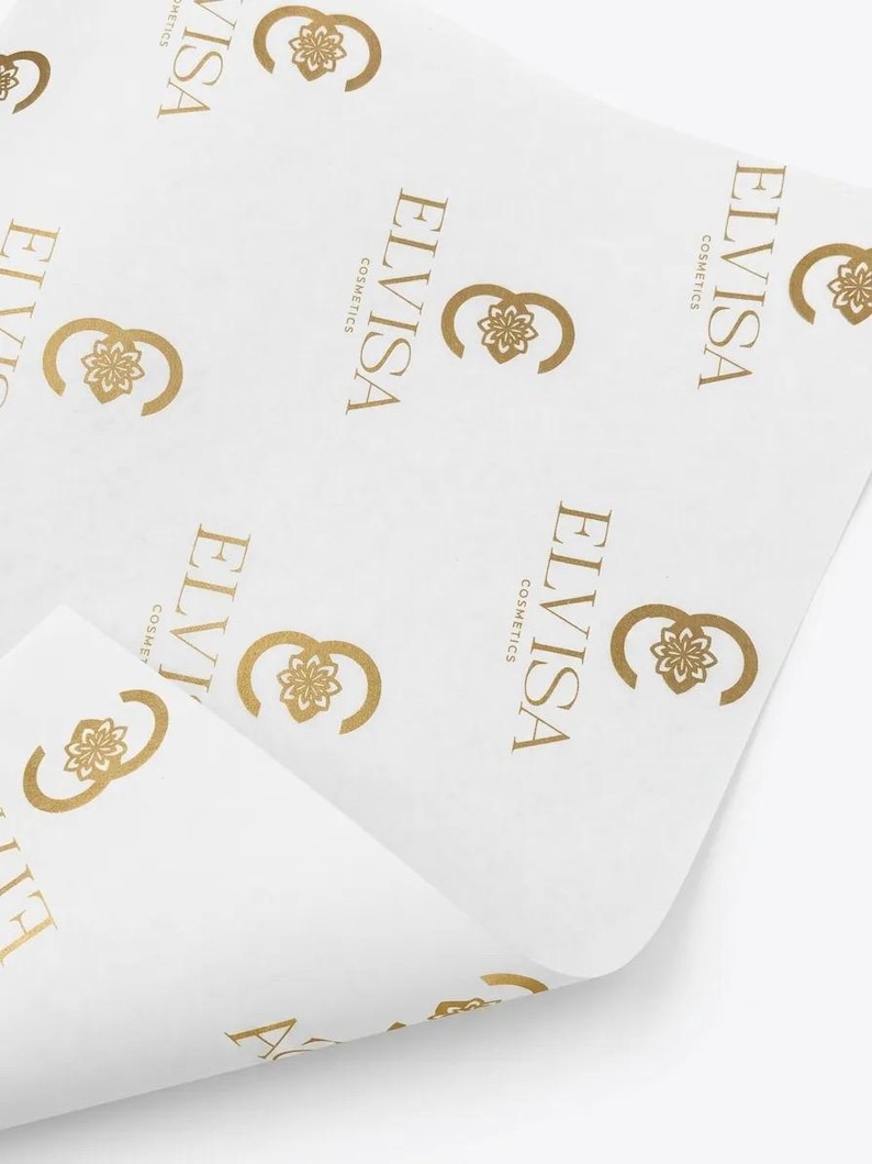 May include: A sheet of white tissue paper featuring a repeating pattern of the gold-colored logo for ELVISA COSMETICS. The logo consists of a stylized floral emblem next to the text ELVISA COSMETICS printed in a clean, sans-serif font.