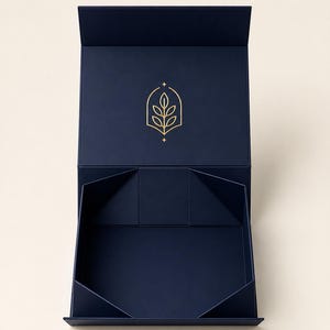 Pode incluir: Uma caixa de presente retangular azul-marinho profundo com tampa articulada. O interior da tampa apresenta um logótipo de linhas douradas de uma folha dentro de uma forma de arco pontiagudo com pequenas estrelas acima e abaixo.
