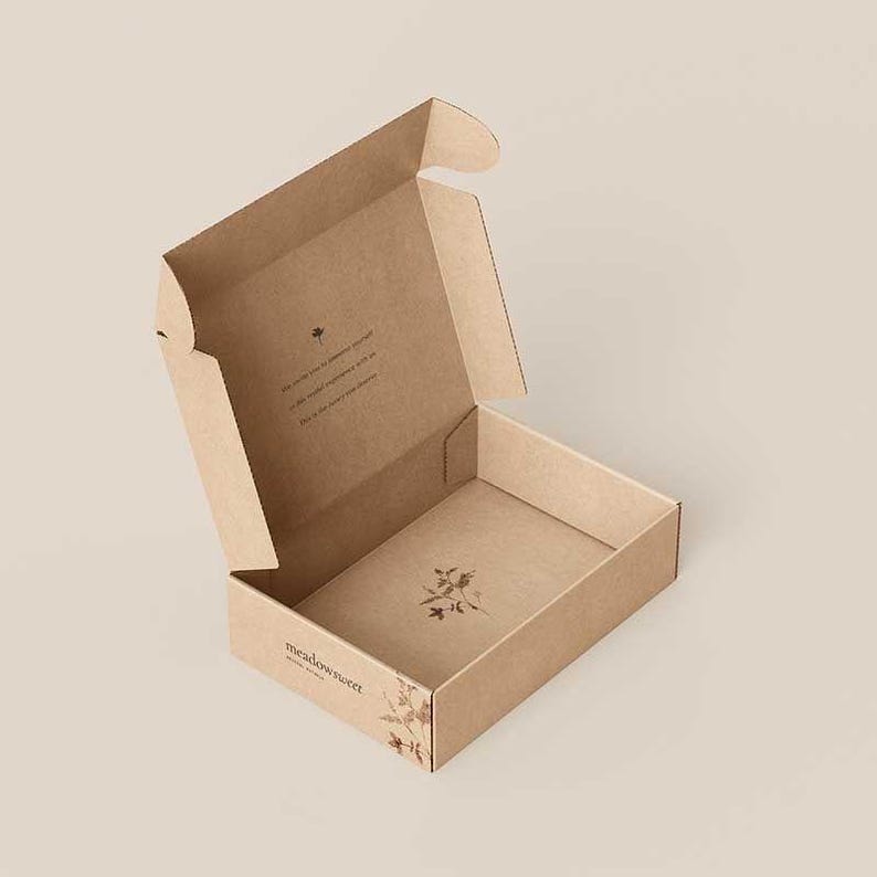 May include: A light brown cardboard shipping box with an open lid. The exterior features the text meadowsweet and a small botanical illustration. The interior base has a floral graphic, and the inside lid contains printed text and a small flower icon.