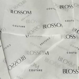 May include: White tissue paper featuring a repeating black print of the word Blossom followed by the word Couture. The text appears in various orientations, including some instances that are mirrored or partially obscured by folds in the paper.