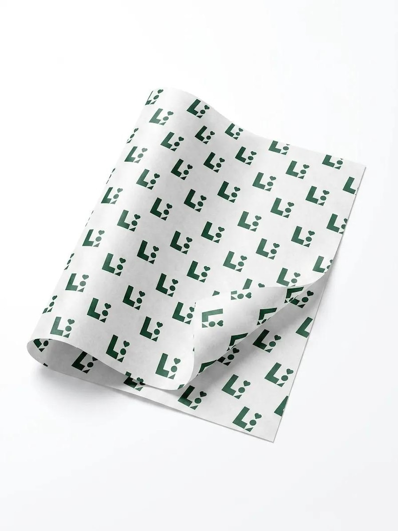 May include: A sheet of white tissue paper featuring a repeating pattern of dark green logos. Each logo consists of a capital letter L, a small solid circle, and a small heart shape arranged in a compact, geometric formation across the surface.