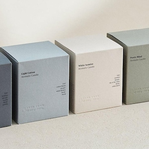 Pode incluir: Quatro caixas quadradas de velas aromáticas Zara Home em fila. As caixas são em tons de cinza, branco e verde. Cada caixa tem o nome da vela impresso na frente. As caixas são rotuladas como "Light Cotton", "White Jasmine" e "Poetic Mind".