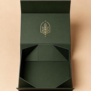 Könnte beinhalten: Eine dunkelwaldgrüne, rechteckige Geschenkbox mit offenem Klappdeckel. Auf der Innenseite des Deckels befindet sich ein goldenes Linienlogo eines Blattes in einem bogenförmigen Rahmen. Die Box hat eine matte Oberfläche und ein faltbares Design.