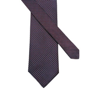 Peut inclure: Une cravate présentant un motif tissé bordeaux foncé et bleu marine avec de petits accents répétitifs en forme de tirets bleu clair disposés en grille diagonale. La cravate a une pointe et un pan large, montrant une texture en tissu.