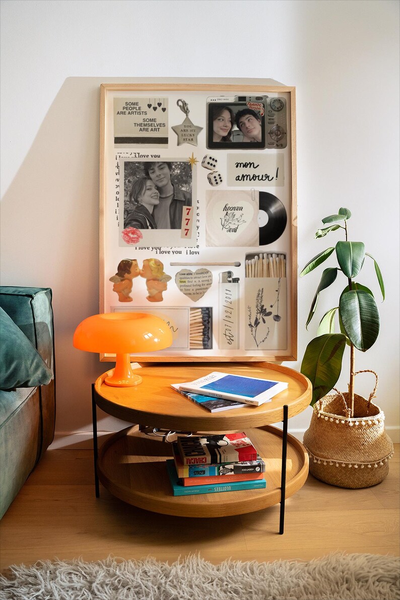 Op de afbeelding: Een houten collage met foto's, een vinylplaat en decoratieve items. Een feloranje paddenstoellamp staat op een houten bijzettafel met twee niveaus. Een potplant in een geweven mand staat naast de tafel.