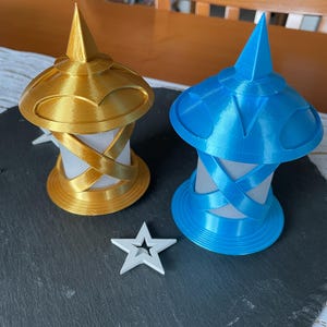 May include: Two decorative lanterns, one gold and one blue, with a star-shaped accent. The lanterns have a cylindrical base with a conical top. The gold lantern is on the left, and the blue lantern is on the right.
