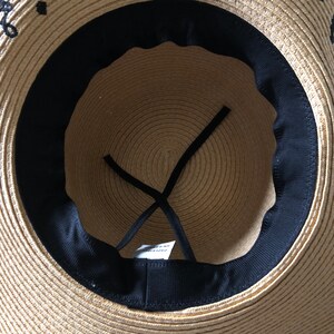 May include: The inside of a straw hat with a black ribbon and a black fabric band around the crown. The hat is made of woven straw and has a brown color.