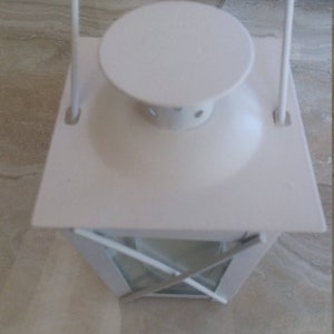 May include: White metal lantern with a glass window and a handle. The lantern has a white metal top with a round opening.