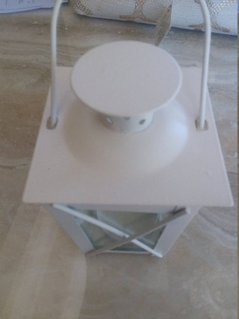 May include: White metal lantern with a glass window and a handle. The lantern has a white metal top with a round opening.