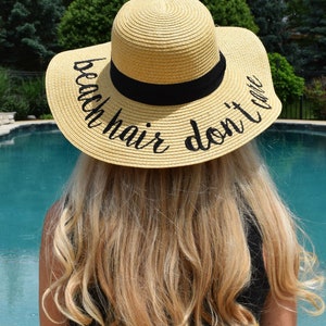 May include: A straw sun hat with a black ribbon and the text "beach hair don't care" embroidered in black.