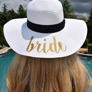 May include: White sun hat with a black ribbon and the word "bride" embroidered in gold on the front.