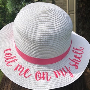 May include: White straw hat with a pink ribbon and the text "Call me on my shell" embroidered in pink.
