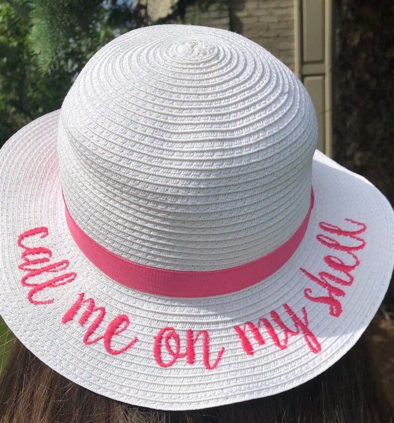 May include: White straw hat with a pink ribbon and the text "Call me on my shell" embroidered in pink.