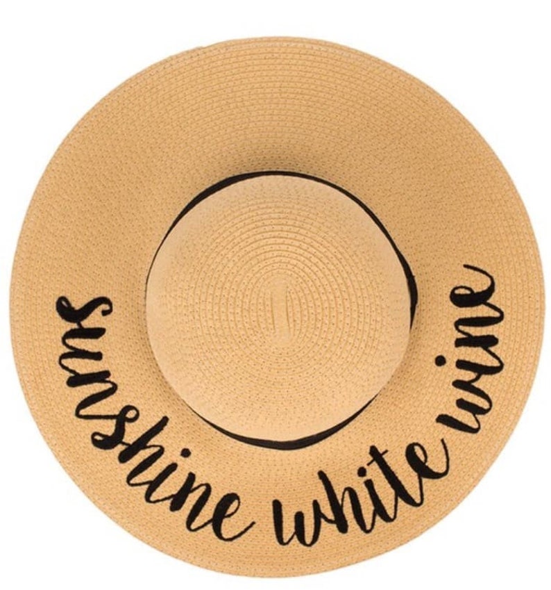 May include: A tan straw sun hat with a black ribbon and the text "Sunshine White Wine" embroidered on the brim.