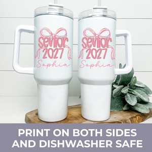 May include: Two white stainless steel tumblers with handles and clear lids. Each features a pink graphic of a bow above the text "senior 2027" and the name "Sophia" in pink script. The design is printed on the front of both insulated cups.
