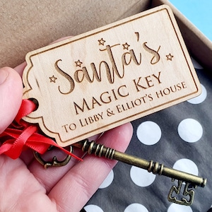 May include: A wooden key tag with the text "Santa's Magic Key To Libby & Elliot's House" and a small, ornate, gold-colored key attached to a red ribbon.