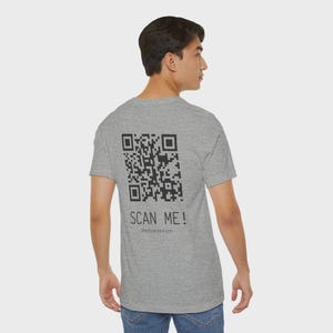 May include: A gray t-shirt with a large black QR code and the words "SCAN ME!" printed on the back. The website address ShopScanWear.com is printed below the text. The shirt is made of a soft material.
