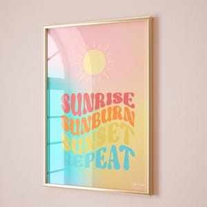 Peut inclure: Impression d'art encadrée avec un fond dégradé rose, jaune et bleu. L'impression présente un soleil jaune et les mots "Sunrise Sunburn Sunset Repeat" dans une typographie rétro colorée. Le cadre est doré.