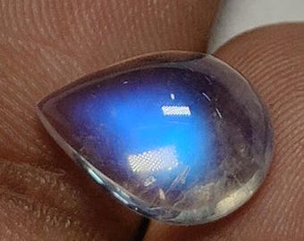 May include: A pear-shaped, translucent gemstone with a blue and white iridescent glow. The polished surface reflects light, creating a captivating display of color. This gemstone is a beautiful example of natural mineral artistry.