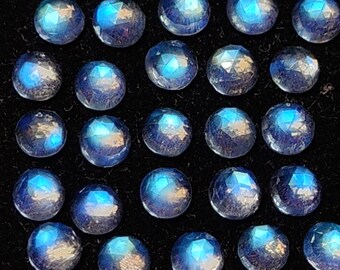 Op de afbeelding: Een verzameling van vierentwintig ronde, gefacetteerde maansteen edelstenen. Elke steen heeft een blauwe iriserende glans, tegen een zwarte achtergrond. Deze edelstenen zijn ideaal voor het maken van sieraden.