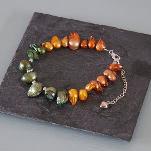 May include: A necklace made of green, gold and orange iridescent pearls. The pearls are strung on a silver chain with a heart-shaped clasp.