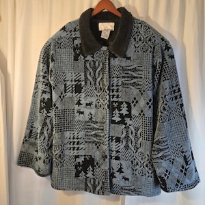 May include: A button-down jacket with a black and blue patchwork design featuring moose and tree patterns. The jacket has a black faux fur collar and is hanging on a wooden hanger.