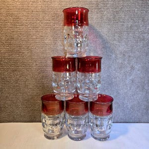 Puede incluir: Seis vasos transparentes con borde rojo, apilados en pirámide. Los vasos tienen un patrón texturizado en forma de burbujas en los lados. Los vasos están dispuestos en forma de pirámide, uno arriba, dos en el medio y tres abajo.