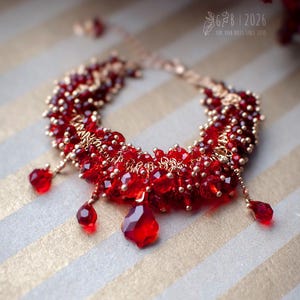 Może przedstawiać: Ręcznie robiona czerwona bransoletka ze złotymi akcentami. Bransoletka składa się z fasetowanych czerwonych koralik&oacute;w i mniejszych złotych koralik&oacute;w, z trzema czerwonymi zawieszkami w kształcie łezki. Tło to wz&oacute;r w złote i białe paski.