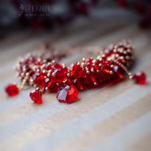 Może przedstawiać: Czerwony naszyjnik z koralik&oacute;w ze złotymi akcentami i wiszącymi czerwonymi kryształowymi zawieszkami. Biżuteria jest umieszczona na tle w paski, z rozmytym elementem kwiatowym w tle.